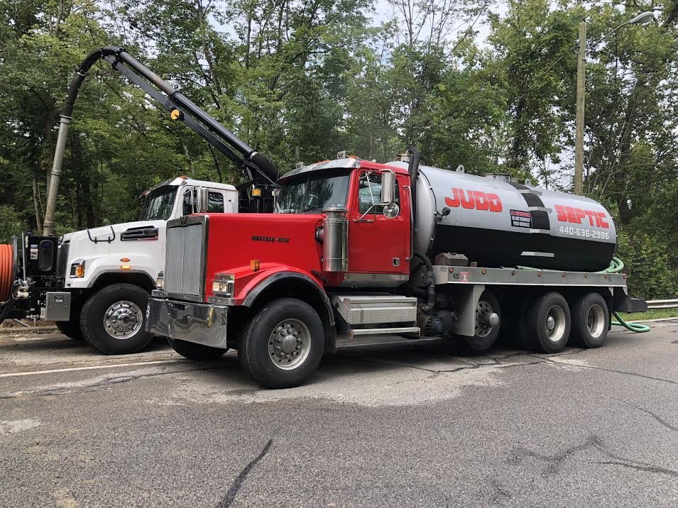 A Judd Septic Tank Cleaning truck is ready for septic tank service, parked beside another truck on a quiet road.